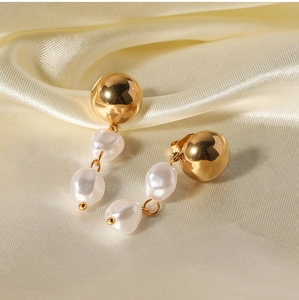 Detailed view of golden ball studs with white baroque pearl tassels on beige silk fabric
