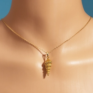 Detail einer goldenen Muschel-Halskette getragen von einem Model vor blauem Hintergrund