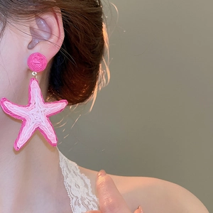 Close-up of a pink woven raffia starfish earring worn by a model for a beach vacation style
