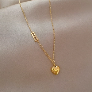 Detail of gold titanium steel H letter and heart pendant on silk background