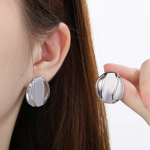 Detailed view of polished silver textured round earrings worn by a female model