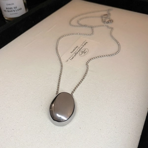 Detail of silver oval pendant on bead chain over beige linen with perfume background