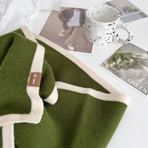 Close-up of green knit scarf texture with white trim and brown decorative brand label