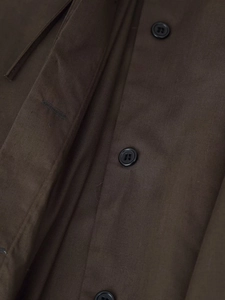 Detailed close-up of dark brown fabric texture and black buttons on the dress