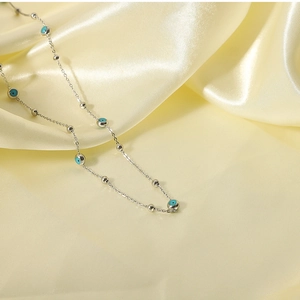 Detailed macro view of silver beaded necklace with turquoise evil eye charms on silk