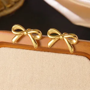 Close-up of polished gold bow stud earrings on a wooden display for a sweet minimalist style