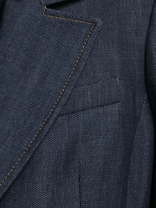 Dettaglio di un blazer in denim blu scuro con cuciture marroni e tasca sul petto