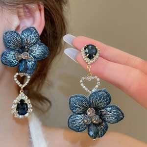 Dettaglio orecchini a fiore blu con anello a cuore scintillante e cristalli a goccia
