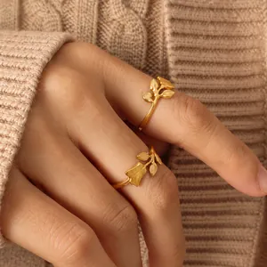 Close-up of golden tulip and leaf rings set against a beige knitted sweater