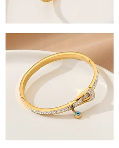 Close-up of gold buckle bangle with zircons and teal pendant on a white ceramic plate