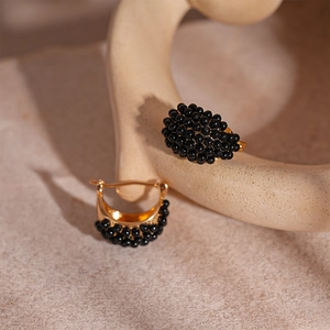 Detail view of retro gold hoop earrings with black beaded texture on stone surface
