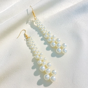 Elegant long pearl tassel earrings featuring white beads on a gold hook over silk fabric