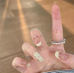 Close-up of sweet French bow press-on nails with green waves, red dots and rhinestones