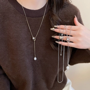 Detail view of heart and pearl layered necklaces on a brown sweater background
