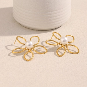 Gros plan de boucles d'oreilles fleurs dorées avec perle centrale sur fond beige