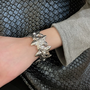 Detail of silver starfish cuff with fluid lava texture and pearl inlay on a model's wrist