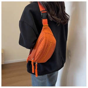 Detail of orange canvas chest bag featuring embroidered text and adjustable strap