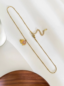 Detail of a gold stainless steel necklace with a pink enamel elephant pendant