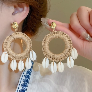 Détail de boucles d'oreilles en raphia tressé avec clous dorés et coquillages blancs