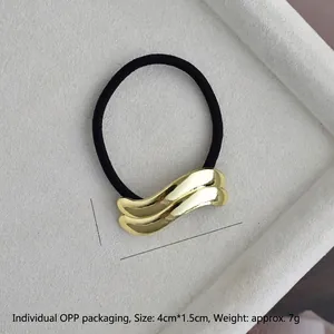Macro detail of wave-shaped golden alloy hair tie with dimensions 4cm by 1.5cm
