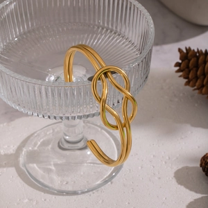 Minimalist knotted open bangle in 18K gold-plated stainless steel on a glass edge