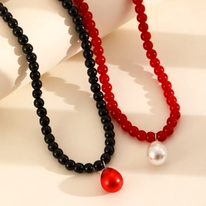 Collar de cuentas con perlas en forma de gota rojas y negras sobre fondo crema suave