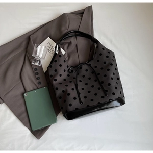 Flat lay of a grey polka dot canvas tote bag with black patent leather base on a blazer