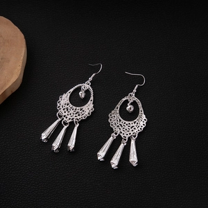 Macro shot of silver hollow drop earrings with leaf tassels on black leather background