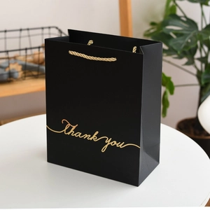 Detail of matte black gift bag with gold Thank You lettering and rope handles