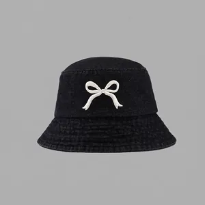 Detail of white bow embroidery on black denim baseball cap with visible twill texture