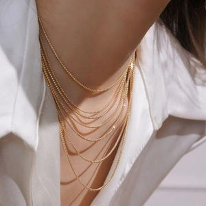 Close-up of layered gold titanium steel necklaces on a model with white shirt background