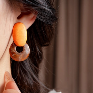 Close-up of geometric resin earrings with orange oval and marble brown circular charms