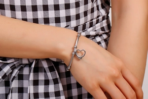 Detailed close-up of a silver open heart charm bracelet worn on a checkered background
