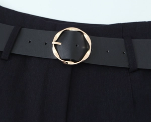 Close-up of black leather belt with a round golden rippled buckle on suit trousers
