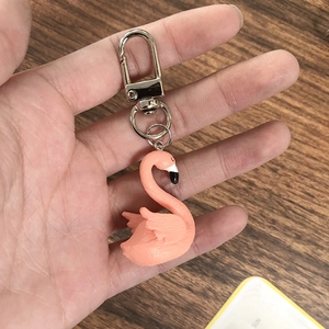 Detail view of a pink flamingo keychain with a sturdy metal ring held by hand