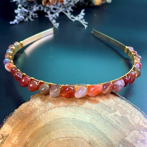 Detailed close-up of handmade gold headband with natural red crystals on wooden block