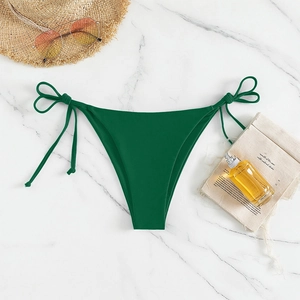 Detail view of dark green side-tie bikini bottom on a white marble beach background