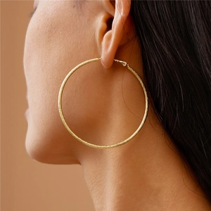 Close-up of a model wearing large gold textured hoop earrings with a matte finish