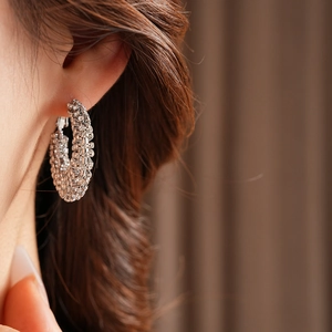 Close-up of a silver-tone hollow hoop earring with micro-paved crystals on a model's ear