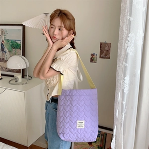 Close-up of quilted heart pattern and brand label on lavender tote bag with yellow strap