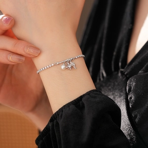 Detail of silver tennis bracelet with pearl, snowflake, and key charms on wrist
