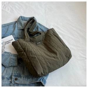 Detail of army green quilted nylon tote bag placed on denim jacket, showing texture