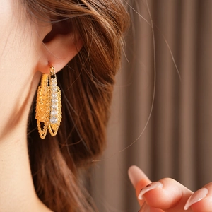 Close-up of gold-plated geometric hoop earrings with layered chains and sparkling cubic zirconia