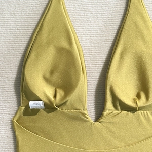 Detail of glossy mustard yellow one-piece swimsuit fabric with gathered cups and care label