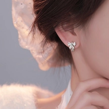 Close-up of silver bow stud earrings with metallic luster on a female earlobe