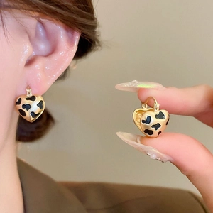 Macro detail of gold-plated leopard print heart earrings held for texture display