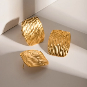 Macro detail of square gold earrings with geometric ripple texture and metallic luster