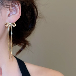 Nahaufnahme eleganter goldener Schleifenohrringe mit langen Quasten am Ohr eines Models
