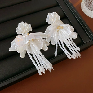 Macro shot of white petal earrings with beaded tassels on a black jewelry tray
