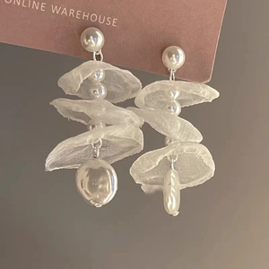 Close-up of white lace floral earrings with layered mesh and baroque pearl tassels